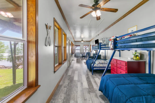 A bright, airy room with bunk beds, blue bedding, and large windows overlooking a grassy area.