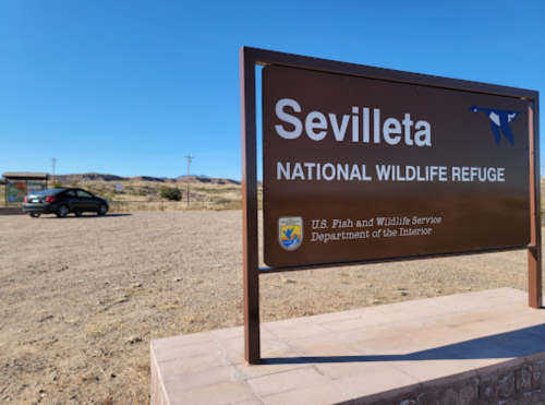 Sign for Sevilleta National Wildlife Refuge with a car parked nearby and a clear blue sky in the background.
