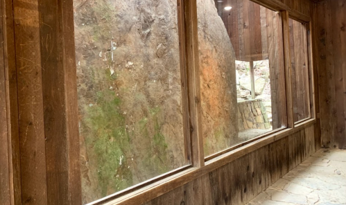 Interior view of a wooden structure with large windows showcasing a rocky landscape outside.