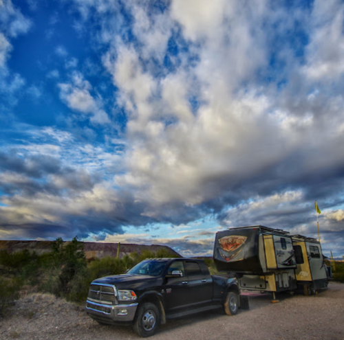A black truck parked next to a travel trailer under a dramatic sky with clouds.