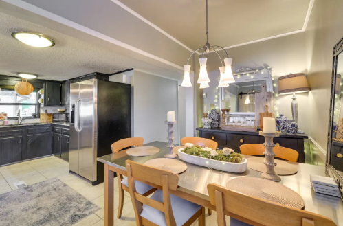 A modern dining area with a wooden table, candles, and a stylish kitchen in the background featuring stainless steel appliances.