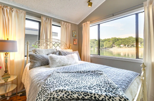 Cozy bedroom with a bed, decorative pillows, and large windows overlooking a serene waterfront view.