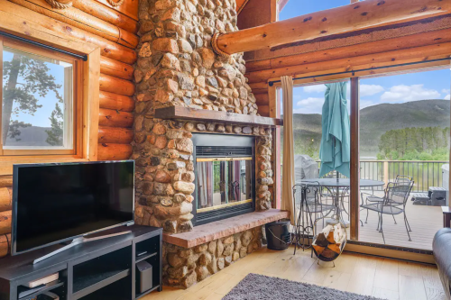 Cozy log cabin interior featuring a stone fireplace, TV, and large windows with mountain views.