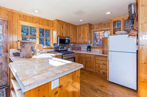 Cozy wooden kitchen with tiled countertops, stainless steel appliances, and natural light from multiple windows.