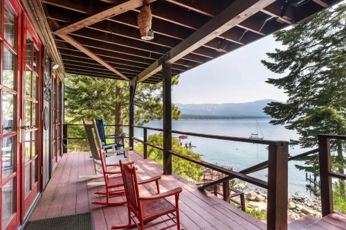 A scenic view from a porch with colorful rocking chairs overlooking a lake and mountains in the background.