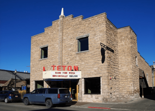 Stone building with a marquee reading "Teton Hand Fired Pizza Organically Delish" against a clear blue sky.