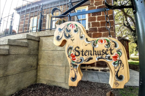 A wooden horse sign with floral designs and the word "Stenhuset" hanging outside a building.
