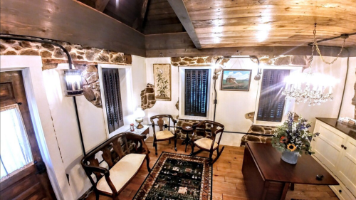 Cozy interior of a rustic room with wooden beams, stone walls, and vintage furniture, featuring a floral arrangement.