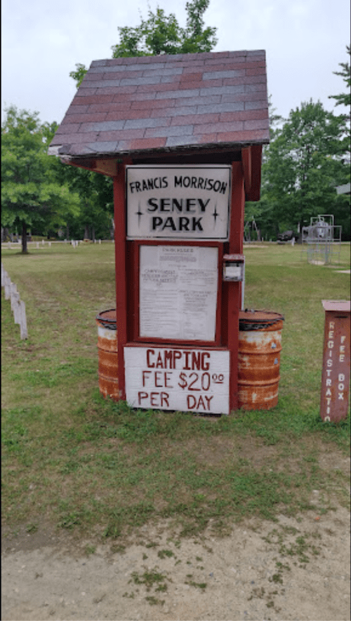 Sign at Seney Park with information about camping fees, $20 per day, displayed on a wooden structure.