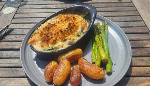 A baked dish with a golden topping, served with roasted potatoes and asparagus on a wooden table.
