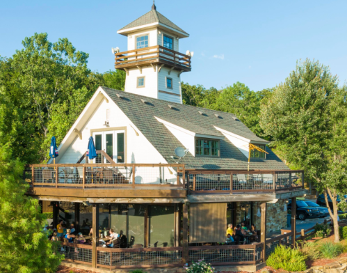 A charming two-story restaurant with a lighthouse-style tower, surrounded by trees and outdoor seating.