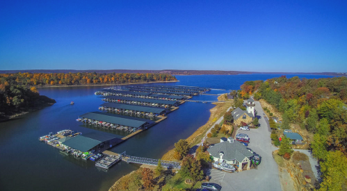 Aerial view of a marina with boats, surrounded by autumn trees and a clear blue sky.