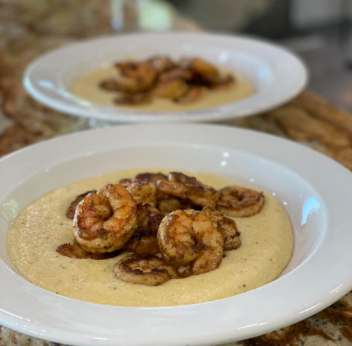 Two plates of creamy grits topped with sautéed shrimp, served on a marble countertop.