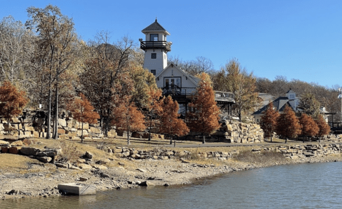 A scenic view of a lighthouse on a rocky shore, surrounded by autumn trees and a clear blue sky.