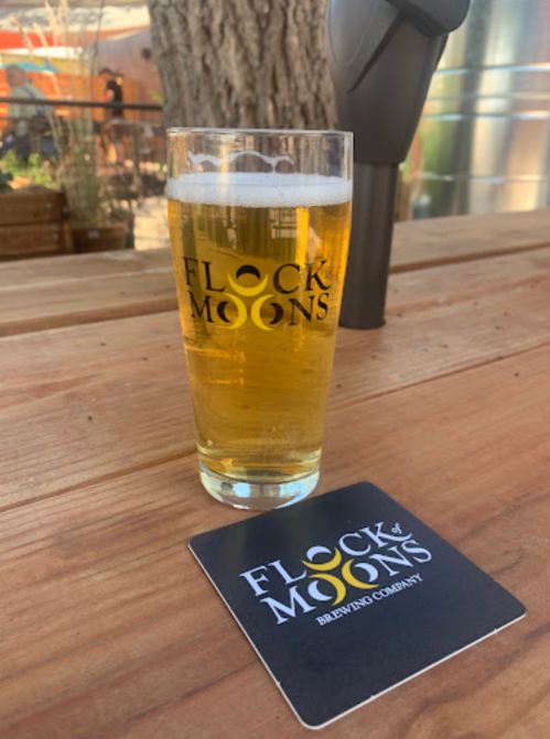 A glass of beer on a wooden table next to a coaster for Flock of Moons Brewing Company.