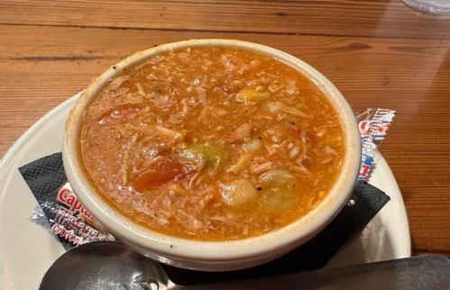 A bowl of hearty soup with rice, vegetables, and a rich broth, served on a plate with a spoon and napkin.