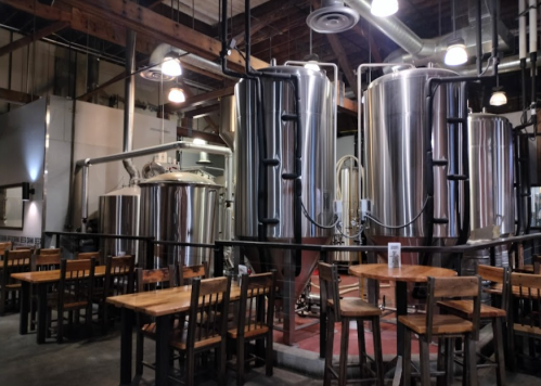 Interior of a brewery featuring large stainless steel tanks and wooden tables for seating.