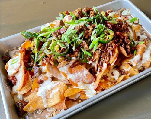 A tray of loaded nachos topped with jalapeños, green onions, and crispy meat, drizzled with creamy sauce.