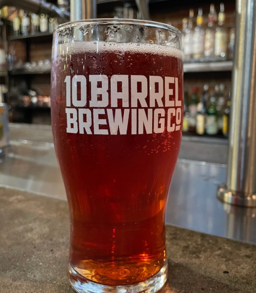 A glass of amber beer from 10 Barrel Brewing Co. sits on a bar counter with blurred bottles in the background.