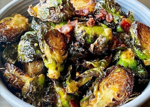 A close-up of crispy roasted Brussels sprouts with bits of bacon in a blue bowl.