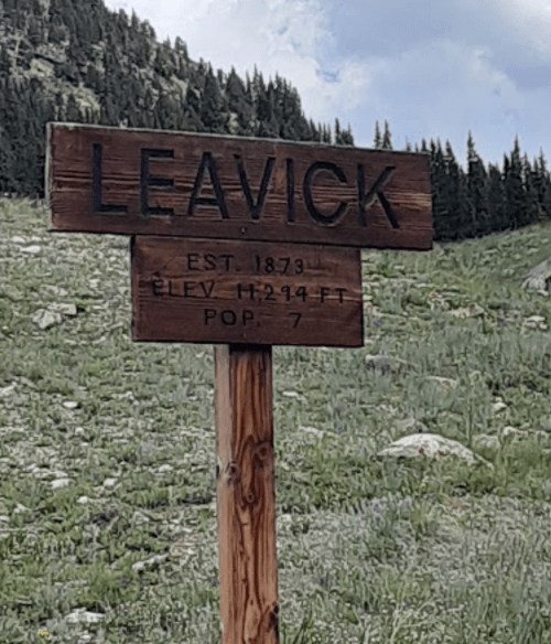 Sign for Leavick, established 1873, elevation 12,294 ft, population 7, surrounded by green hills and trees.