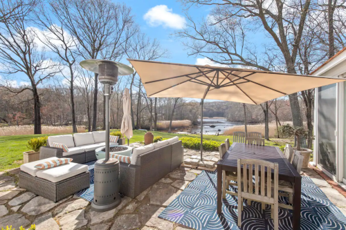 A serene outdoor patio with a dining table, seating area, and an umbrella, overlooking a tranquil landscape.