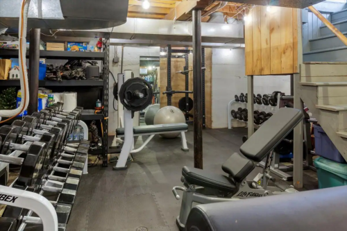 A home gym with weights, a bench, exercise ball, and various fitness equipment in a basement setting.