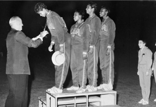 A group of athletes receiving medals on a podium, with a man presenting a medal to one of them. Black and white photo.