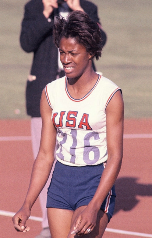 A female athlete in a USA uniform walks on a track, looking focused and determined.