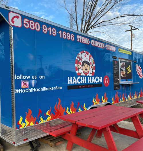 A food truck with a blue exterior featuring the name "Hachi Hachi" and images of steak, chicken, and shrimp.