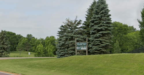 Sign for East Brainerd Regional Park surrounded by green trees and grass on a cloudy day.