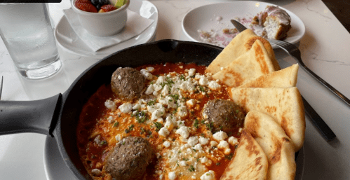 A skillet with meatballs, cheese, and pita bread, alongside a dessert and a bowl of mixed berries.