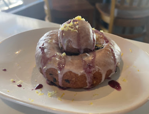 A glazed donut topped with a scoop of ice cream and drizzled with berry sauce, garnished with lemon zest.