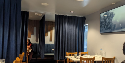 A cozy restaurant interior with blue curtains, wooden accents, and a TV displaying an underwater scene.