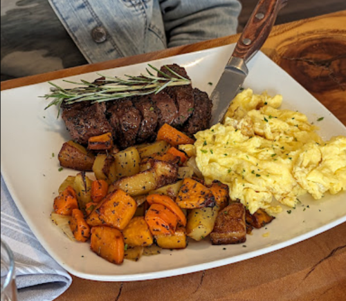 A plate of steak with rosemary, scrambled eggs, and roasted potatoes and carrots.