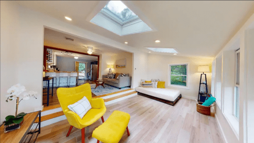 Bright, modern living space with yellow chairs, skylights, and a cozy atmosphere, featuring a seamless flow to the kitchen.