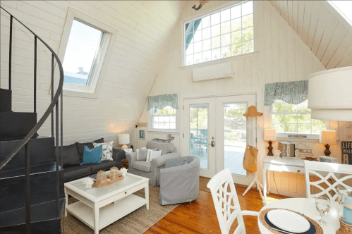 Cozy, modern living room with a spiral staircase, large windows, and light-colored furniture in a bright, airy space.