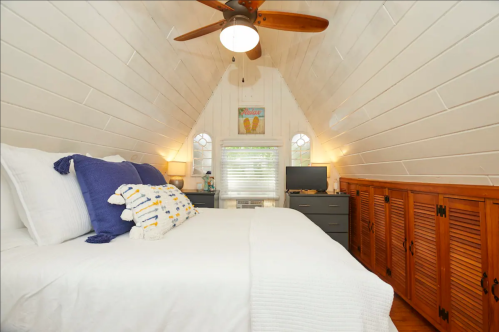 Cozy bedroom with a sloped ceiling, white walls, a ceiling fan, and wooden furniture, featuring a bed and a TV.
