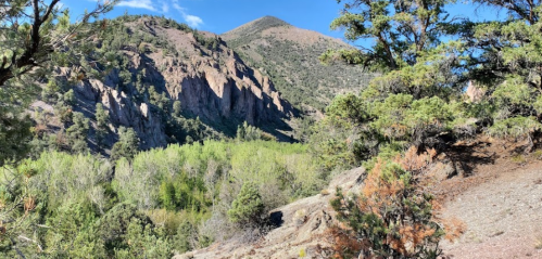 A scenic view of rugged mountains surrounded by lush greenery and trees under a clear blue sky.