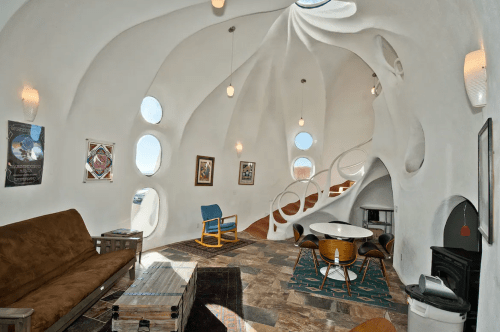 A unique, modern interior with organic shapes, circular windows, and a cozy living area featuring a sofa and dining table.