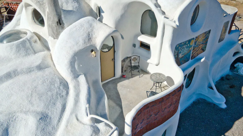 A unique, sculptural white house with rounded shapes and a small patio featuring a table and chair.