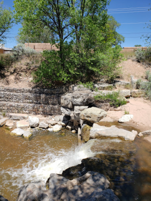 A serene river scene with rocks and greenery, featuring a small waterfall and a sandy bank.