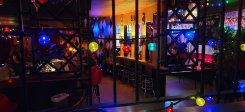 A vibrant bar scene with colorful lights, seating, and patrons enjoying the atmosphere through a decorative window.