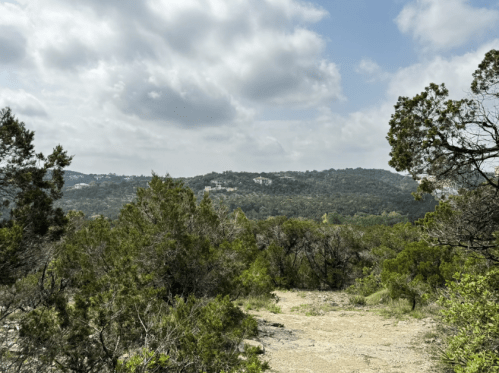 A scenic view of a lush, green landscape with trees and hills under a partly cloudy sky.