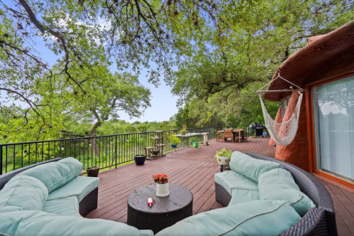 A spacious deck with cozy seating, potted plants, and a hammock, surrounded by lush greenery and trees.