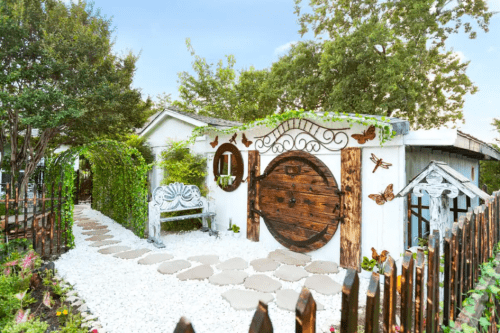 Charming garden entrance with a wooden door, stone path, and decorative elements surrounded by greenery.