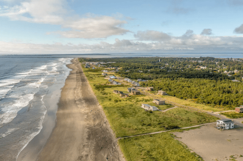 Aerial view of a coastal area with sandy beach, waves, and a small town surrounded by greenery.
