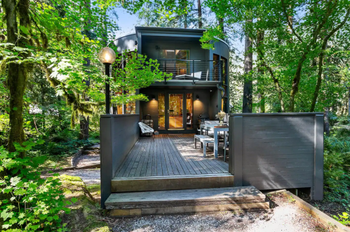 Modern house surrounded by lush greenery, featuring a wooden deck and large windows for natural light.