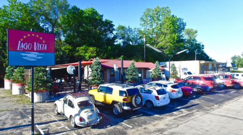 A restaurant named Lago Vista with outdoor seating, surrounded by trees and a parking lot filled with various cars.