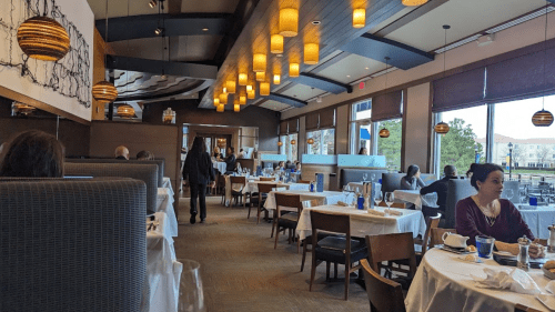 A modern restaurant interior with tables set for dining, warm lighting, and patrons enjoying their meals.